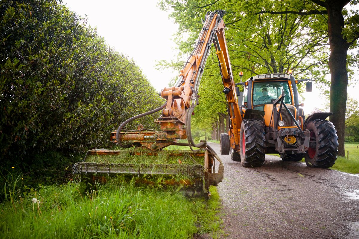 Traktor mäht Seitenstreifen an Weg